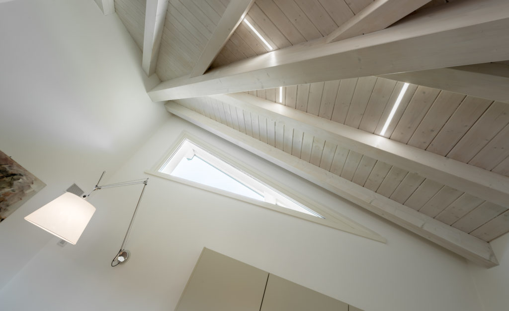 Le linee delle travi del tetto si incontrano in un punto focale e si rispecchiano nel taglio luminoso della finestra.